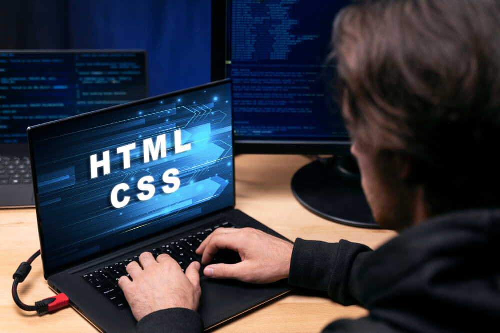 A man typing on a laptop with HTML and CSS text on the screen
